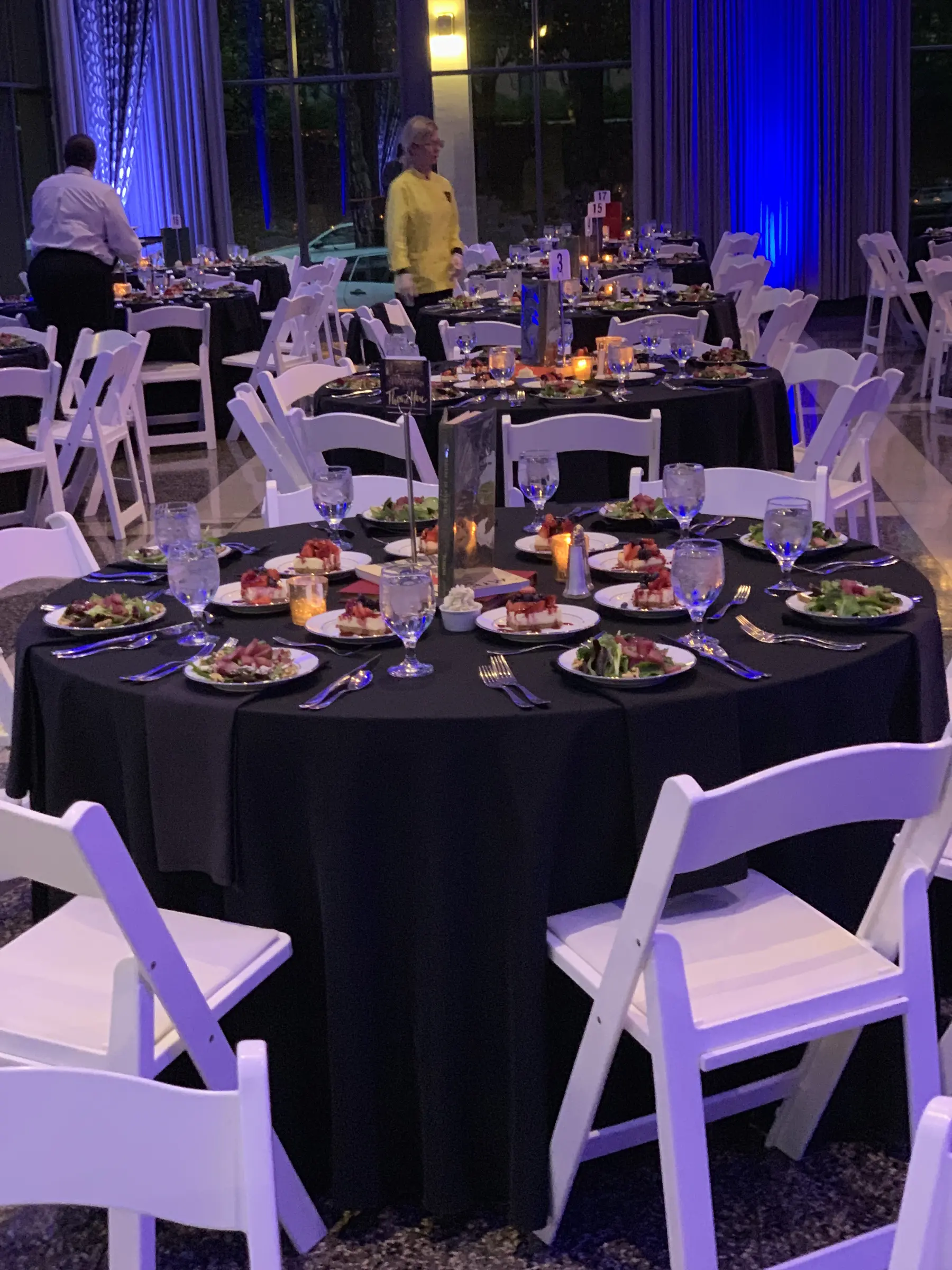 An evening dining room set with round tables, plated meals and white chairs.