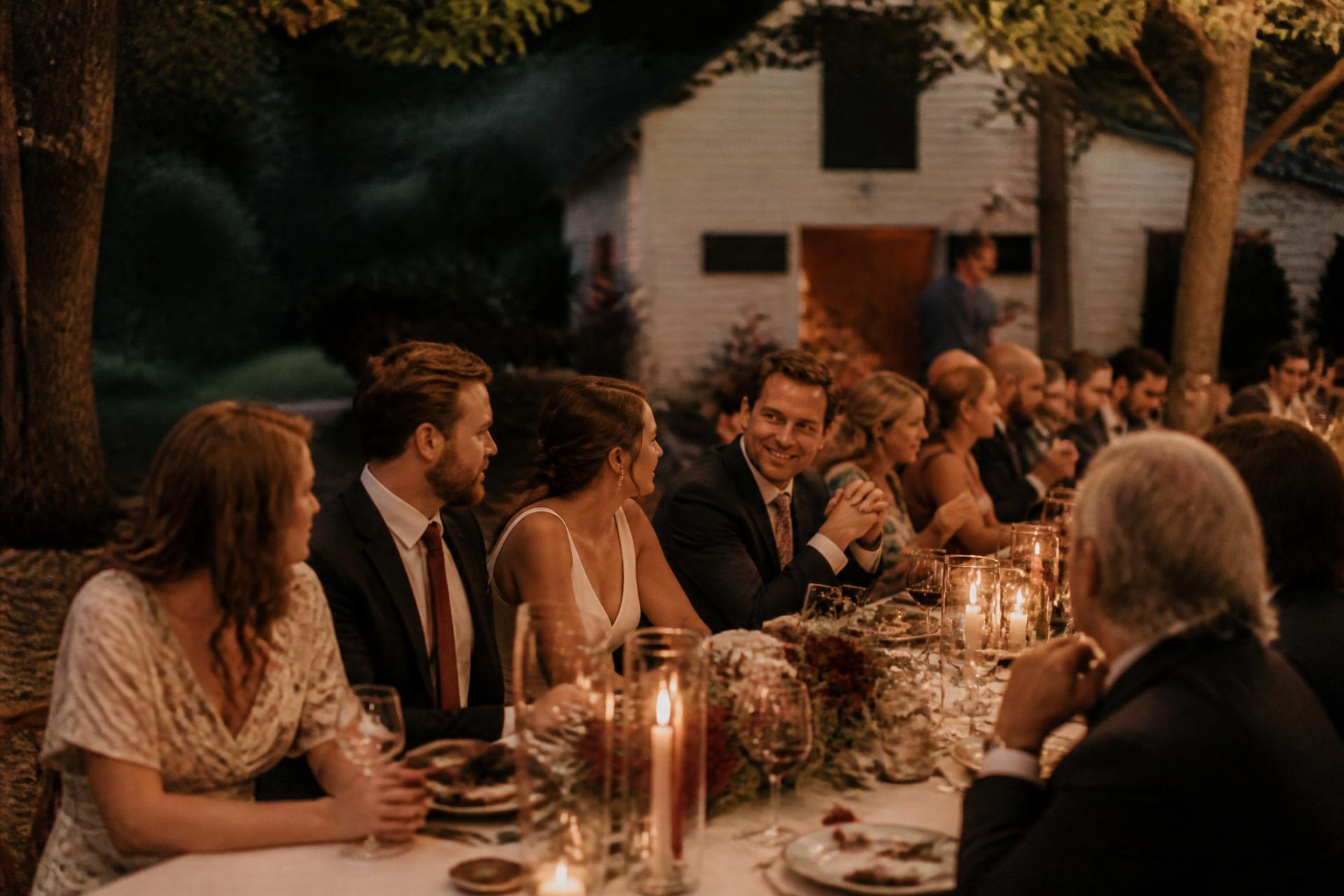 Guests seated along a long candlelit table outdoors at dusk